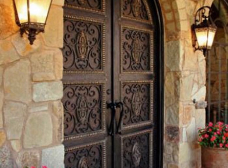Ornate metal door with lanterns on a stone wall.