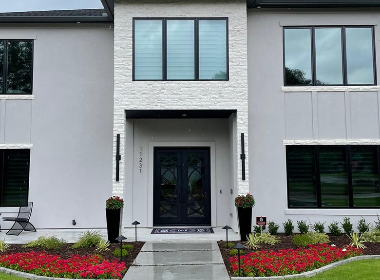 Modern white house with black door and trim, surrounded by a garden with red flowers.